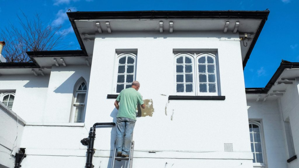 man in greenshirt and blue denim jeans standing on white concrete building during daytime